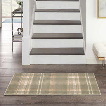 Entryway scene with olive plaid Nourison Grafix rug on dark wood floor, white stairs, and modern decor.