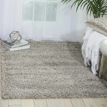 Light grey shag rug in a bright room with white bench, throw blanket, and tropical plant. Nourison Amore rug.