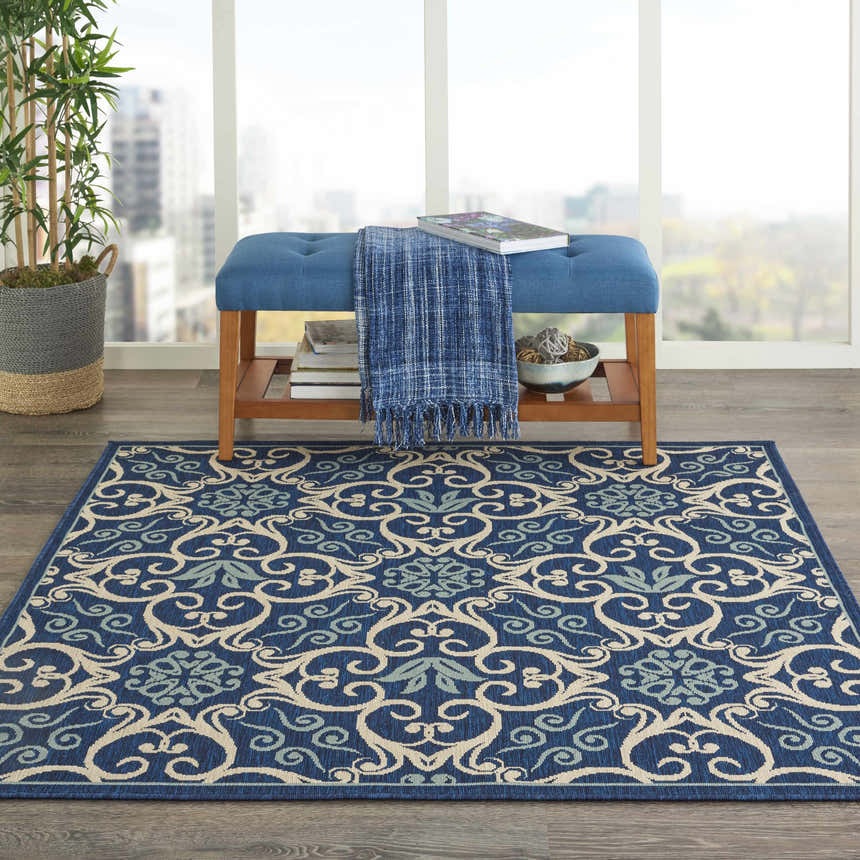 Living room scene with a Nourison Caribbean Navy Contemporary Area Rug, blue bench, and city view.
