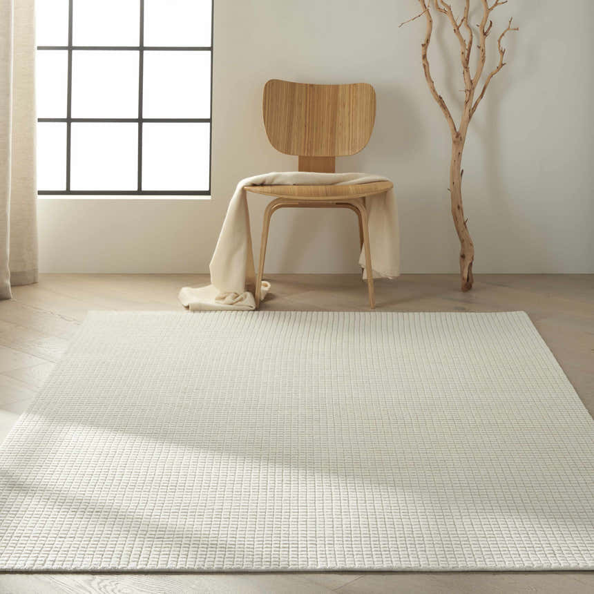 Minimalist room scene with Calvin Klein Pretoria Ivory rug, wood chair, blanket, and tree branch decor.