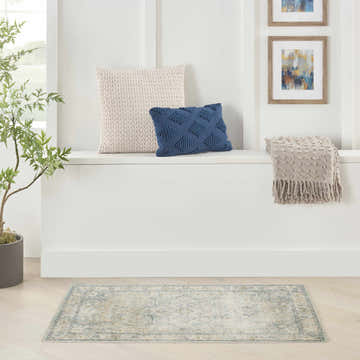 Entryway with a light blue vintage Nourison Astra area rug, white bench, pillows, and artwork.