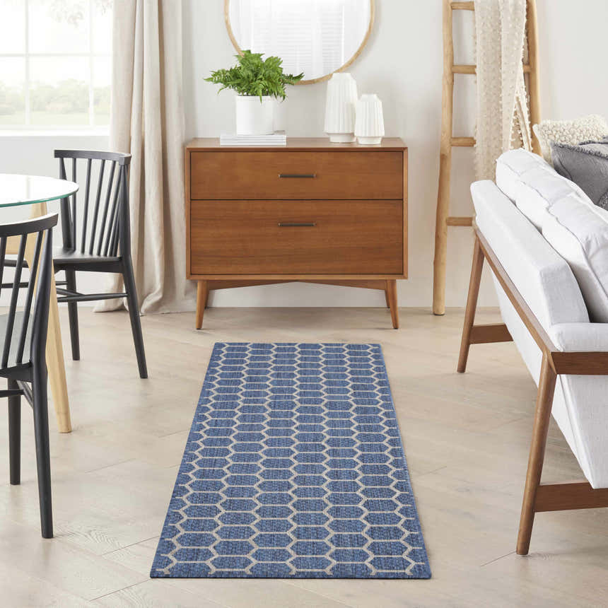 Modern dining room with a Nourison Twist Reversible Blue Area Rug, wood furniture, and white sofa.