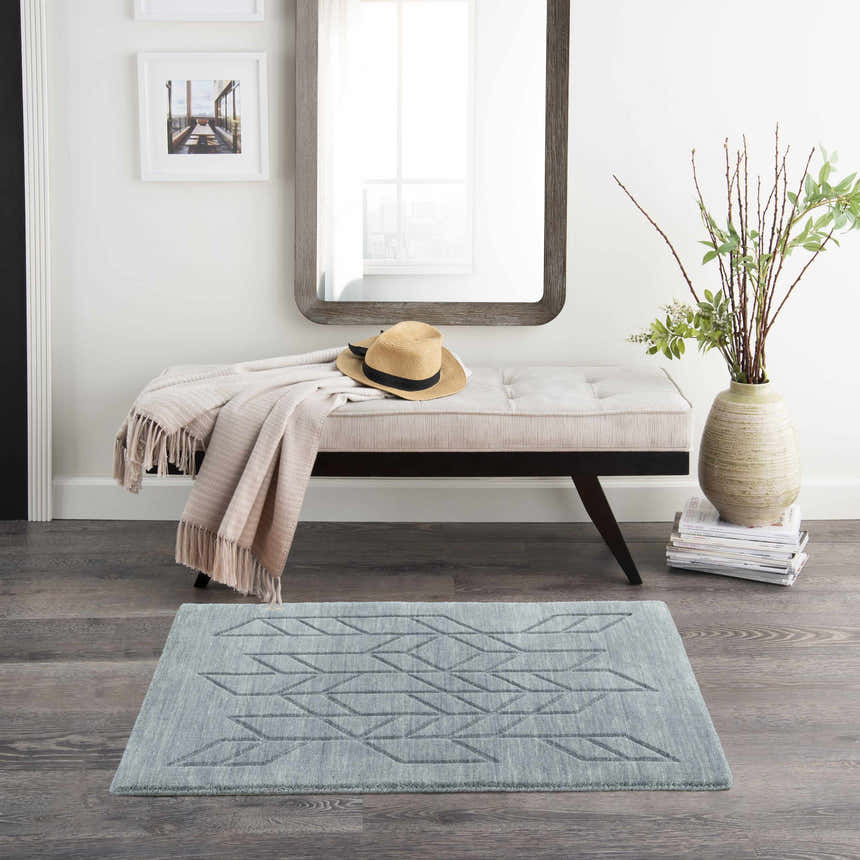 Entryway with light blue Nourison Alessia rug, wood floors, bench with blanket, mirror, and vase with greenery.