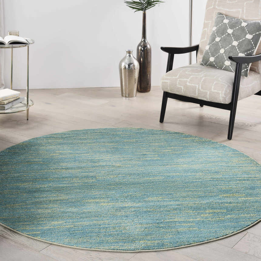 Living room scene with a round Nourison Essentials Blue Green Outdoor Area Rug, chair, and side table.