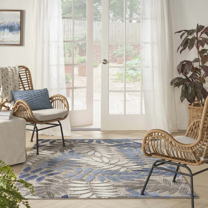 Bright sunroom with a Nourison Aloha Grey Blue Tropical Area Rug, wicker chairs, and sheer curtains.