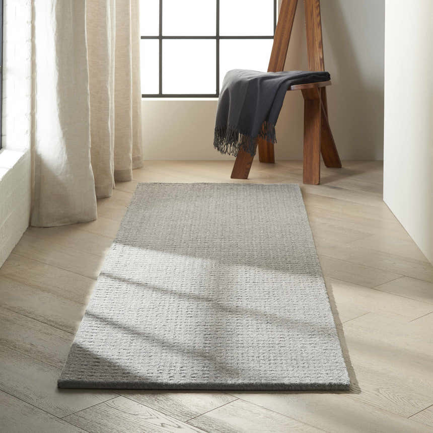 Minimalist room scene with a Calvin Klein Las Vegas Grey Retro runner rug on light wood floors near a window.