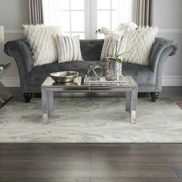 Living room scene with grey sofa, mirrored table, and Inspire Me! Home Décor Elegance Grey rug.