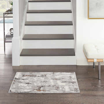 Entryway with Nourison Elation Grey Ivory rug, dark wood floors, white stairs, and a modern white bench.
