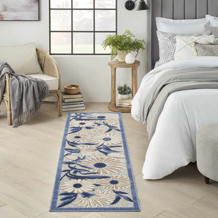 Bedroom scene with Nourison Aloha Blue Grey Outdoor Area Rug runner, floral pattern, blue border, light wood floors, and neutral decor.