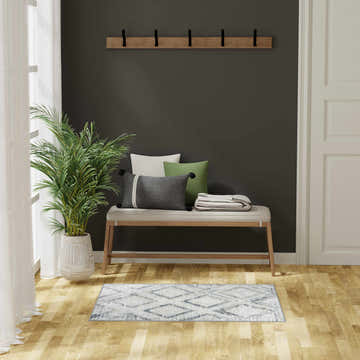 Entryway scene with a Nourison Dekor Grey Navy rug, bench, pillows, and plant. Modern style.