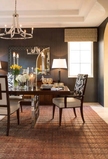 Elegant dining room with Barclay Butera Equestrian Saddle rug, dark walls, crystal chandelier, and set table.