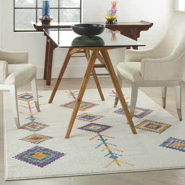 Dining room with Nourison Passion Ivory Multicolor Bohemian Area Rug, glass table, and cream chairs.