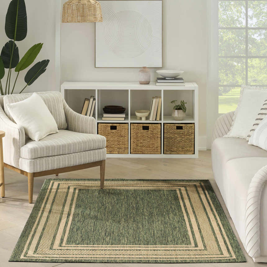 Living room scene with a green Nourison Horizon Indoor/Outdoor Area Rug, striped armchair, white sofa, and shelving unit.
