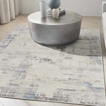 Living room scene with a Calvin Klein CK022 Infinity ivory, grey, and blue area rug under a modern round coffee table.