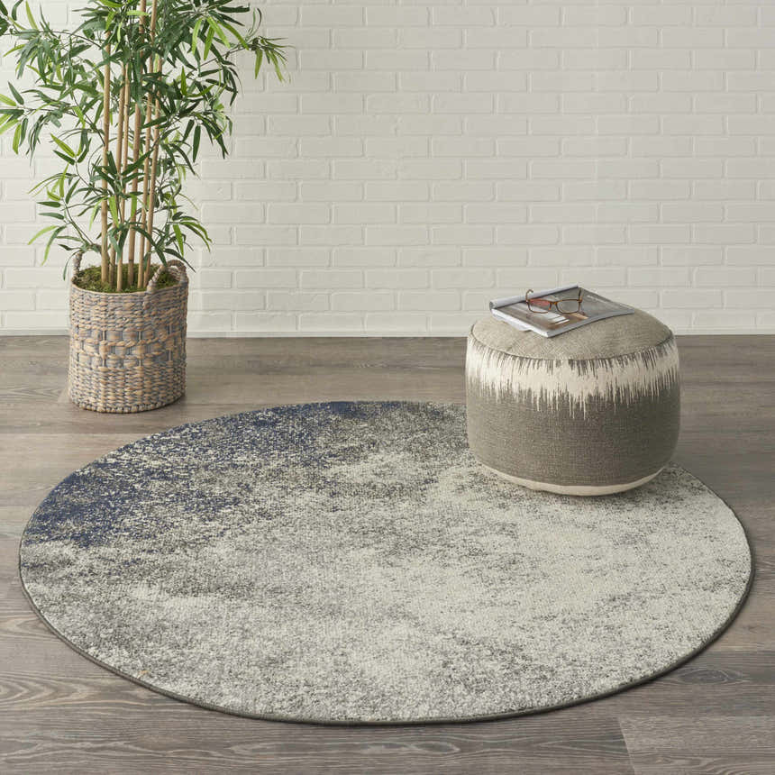 Modern room scene with round Nourison Passion Charcoal Ivory rug, taupe ottoman, and bamboo plant.
