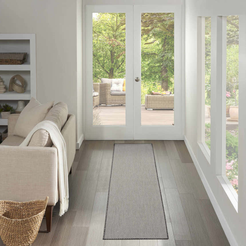Light-filled hallway with a Nourison Courtyard Ivory Charcoal rug leading to an outdoor patio. Neutral tones and modern style.