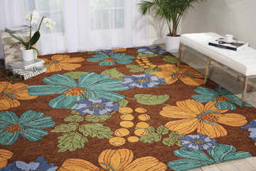 Bright living room scene with floral Nourison South Beach Chocolate Area Rug, white bench, sheer curtains, and potted plants.