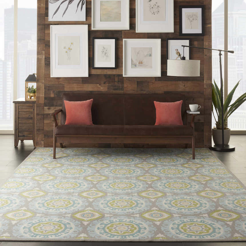 Living room scene with a Waverly Sun N' Shade Jade rug, brown sofa, wood wall, and botanical art. Coastal style.
