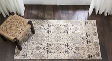 Overhead shot of a Nourison Silver Screen Grey Slate Persian rug on dark wood floors with a woven stool.