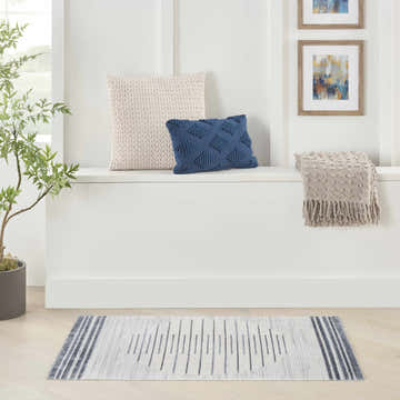 Bright room scene with Nourison Astra Ivory Blue rug, pillows, throw blanket, and plant.