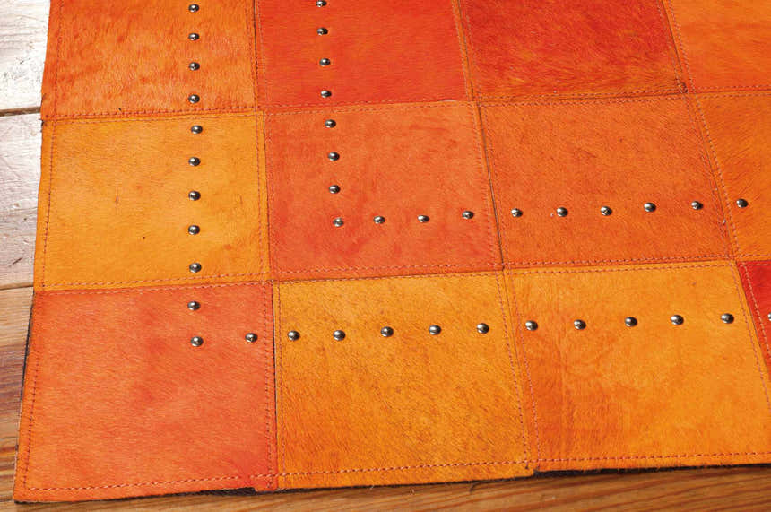 Close-up of the Barclay Butera Medley Tangerine rug. Hair on hide squares with silver nailhead trim. Dark orange tones.