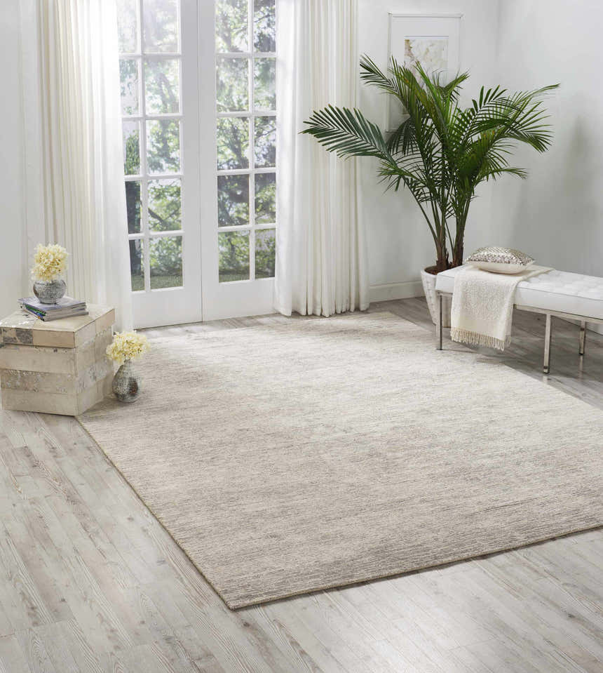 Light-filled room with a Nourison OCEAN Mist rug, white bench, and potted palm. Modern, serene space.