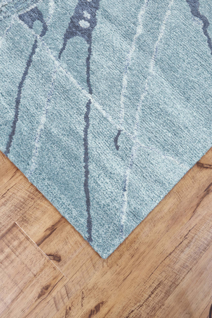 Close up of Feizy Cosmo rug. Blue, green, and gray abstract design on a hand-tufted, transitional area rug. Corner