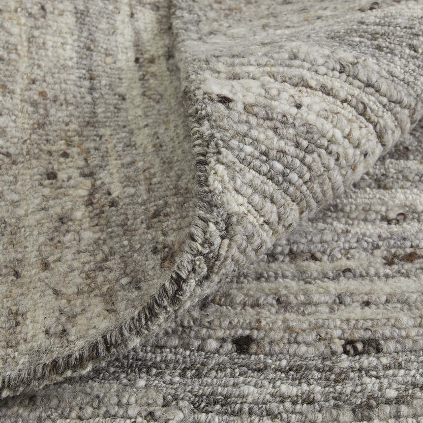Close-up of the hand-woven Feizy Navaro rug. Gray, ivory, and taupe wool and viscose fibers create a textured abstract design. Fold