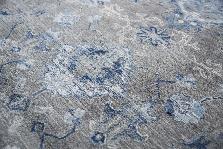 Close-up of the Rizzy GS7225 area rug. Gray rug with a blue and light gray floral and paisley pattern. Machine woven texture. Texture