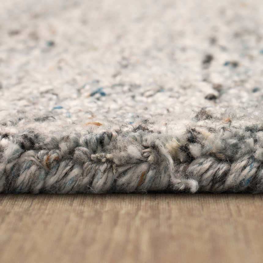 Close-up of the hand-tufted Karastan Haberdasher Silver Area Rug showing texture and colors: gray, ivory, blue, and rust. Pile