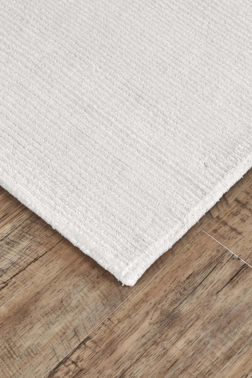Close up of the textured, hand woven Feizy Batisse Modern Solid White rug on wood floors. Corner