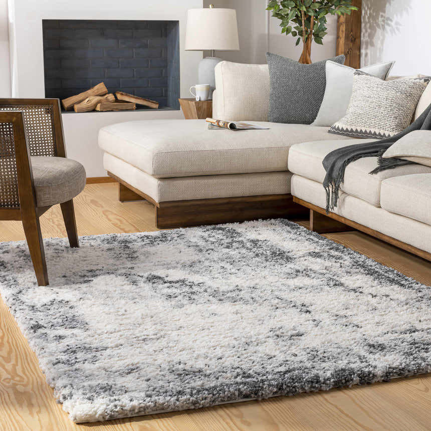 Living room scene with a Hilotongan Plush Abstract Area Rug in black, cream, and gray under a chair and sectional sofa. Roomscene-Rectangle