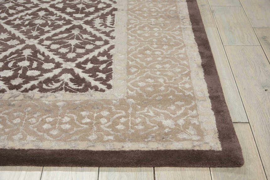 Close-up of the Nourison Symphony Charcoal rug showing taupe floral patterns and a dark brown border on wood floors.