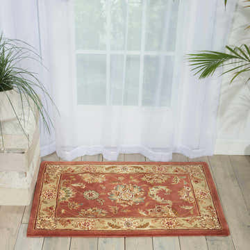 Bright room scene with a Nourison 2000 Rose Persian rug in pink with floral pattern on wood floor near sheer curtains.