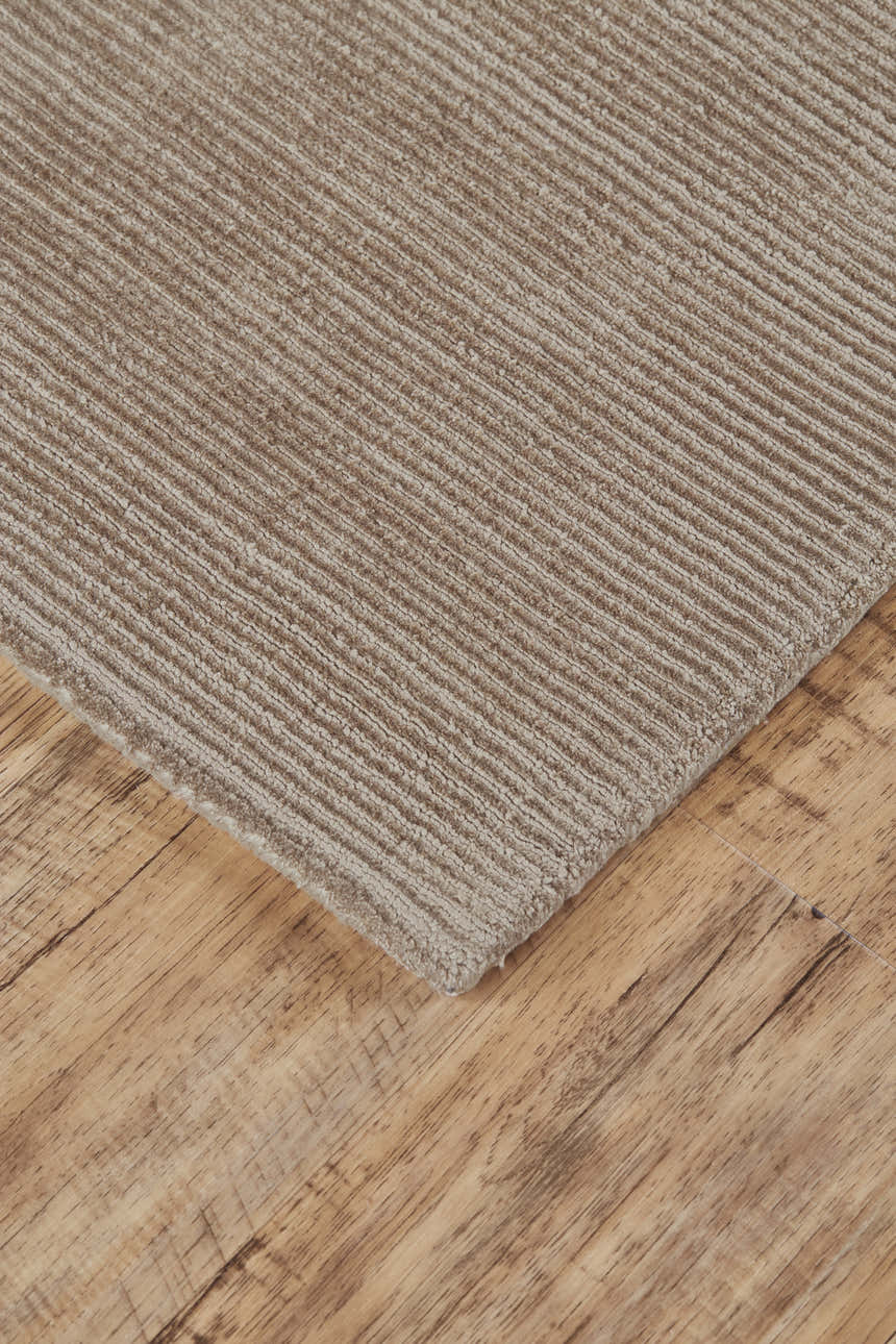 Close-up of the Feizy Batisse Tan/Ivory/Taupe Area Rug showing its ribbed texture and neutral colors on wood floor. Corner