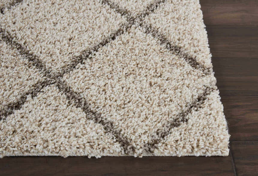 Close-up of the cream Nourison Brisbane shag rug showing its plush texture and geometric diamond pattern on a dark wood floor.
