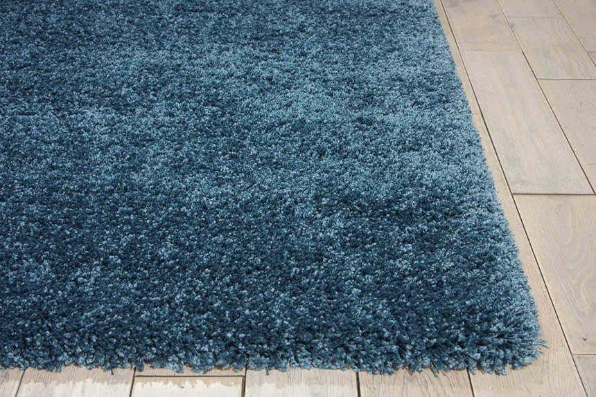 Close-up of the plush Nourison Amore Slate Blue Shag rug showing its texture and color on hardwood flooring.