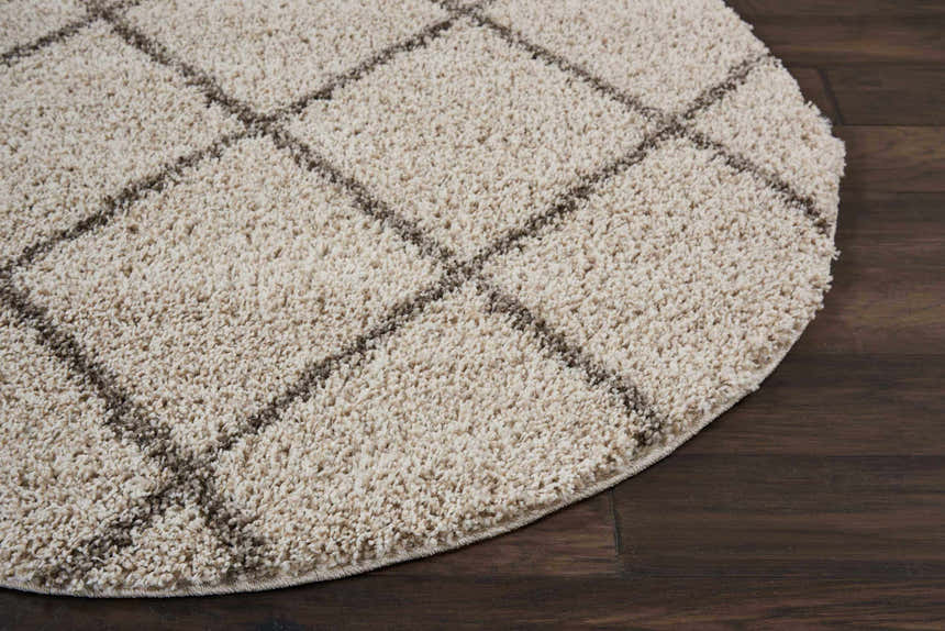 Close-up of a cream shag Nourison Brisbane rug with a diamond pattern on a dark wood floor.