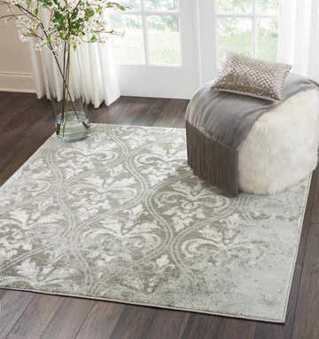 Bright room scene with Nourison Euphoria Grey Vintage rug, white ottoman, and floral arrangement on dark wood floor.