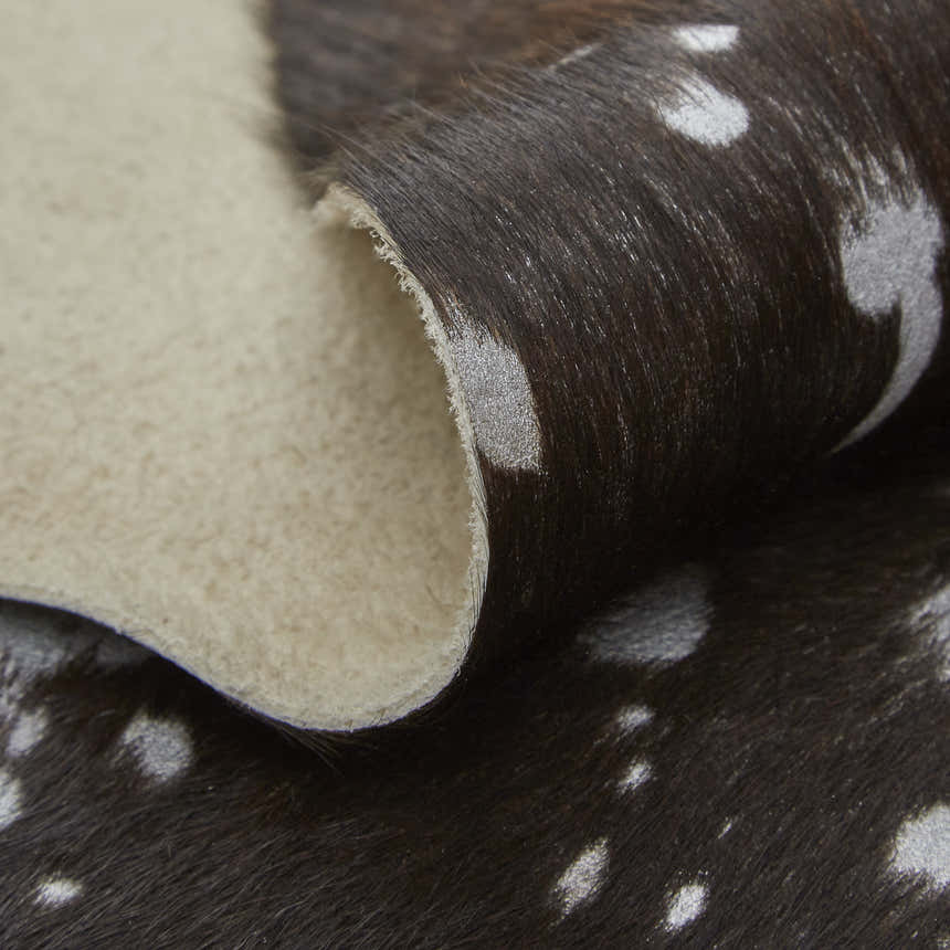 Close-up of the Feizy Ellyse rug. Silver spots pattern the dark brown cowhide. The rug's backing is light tan. Fold