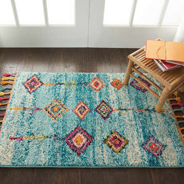 Entryway scene with a Nourison Nomad Aqua Tribal rug, wood floors, and a small bamboo stool with books.