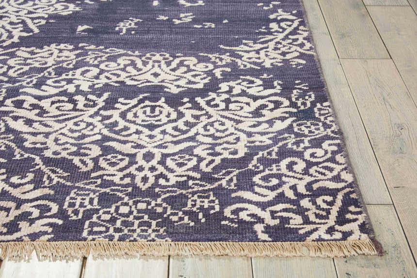 Close-up of Nourison Aldora Royal Vintage rug. Royal purple with ornate ivory floral pattern and fringe detail.