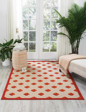 Bright sunroom featuring the Nourison Aloha Red Indoor/Outdoor Area Rug, with red floral pattern, plants, and white furniture.