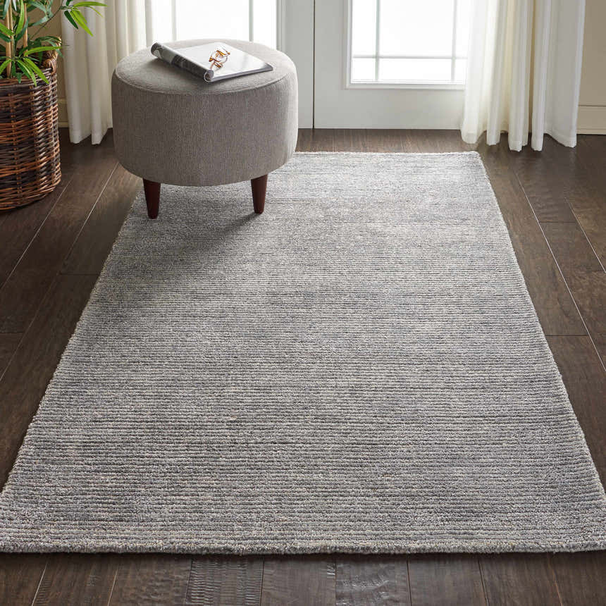 Living room scene with Nourison Weston Silver Birch rug, gray ottoman, dark wood floors, and sheer white curtains.