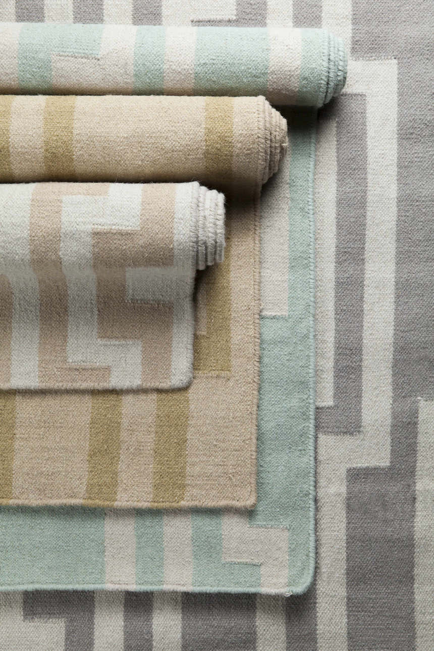 Close-up of rolled Carteret Area Rugs. Wool rugs in ice blue, light beige, and gray with striped and geometric patterns. Styleshot