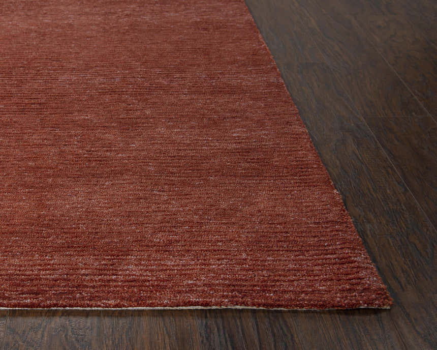 Close-up of the hand-tufted Rizzy MPK101 area rug in dark red and rust on a dark wood floor. Corner