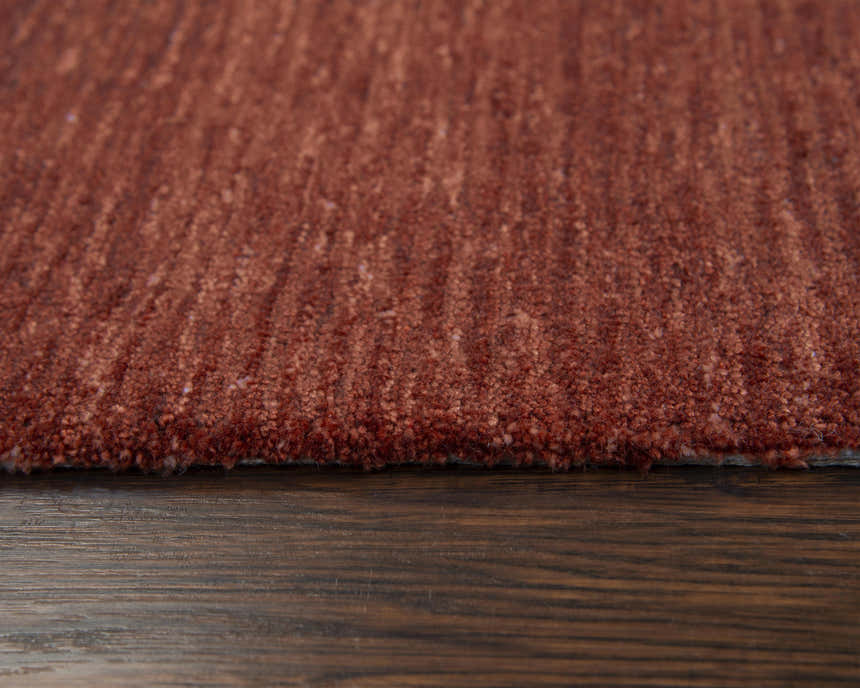 Close-up of the hand-tufted Rizzy MPK101 area rug. The rug is dark red and rust colored with a casual solid design. Pile