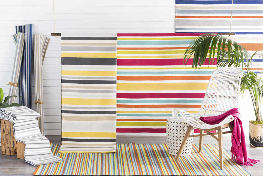 Bright, airy room scene with striped Shawville Area Rugs in colorful, neutral, and blue tones. White chair and palm plant. Styleshot