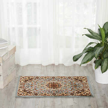 Sunlit room scene with a Nourison Delano Blue Persian rug, sheer curtains, potted plant, and wood floors.