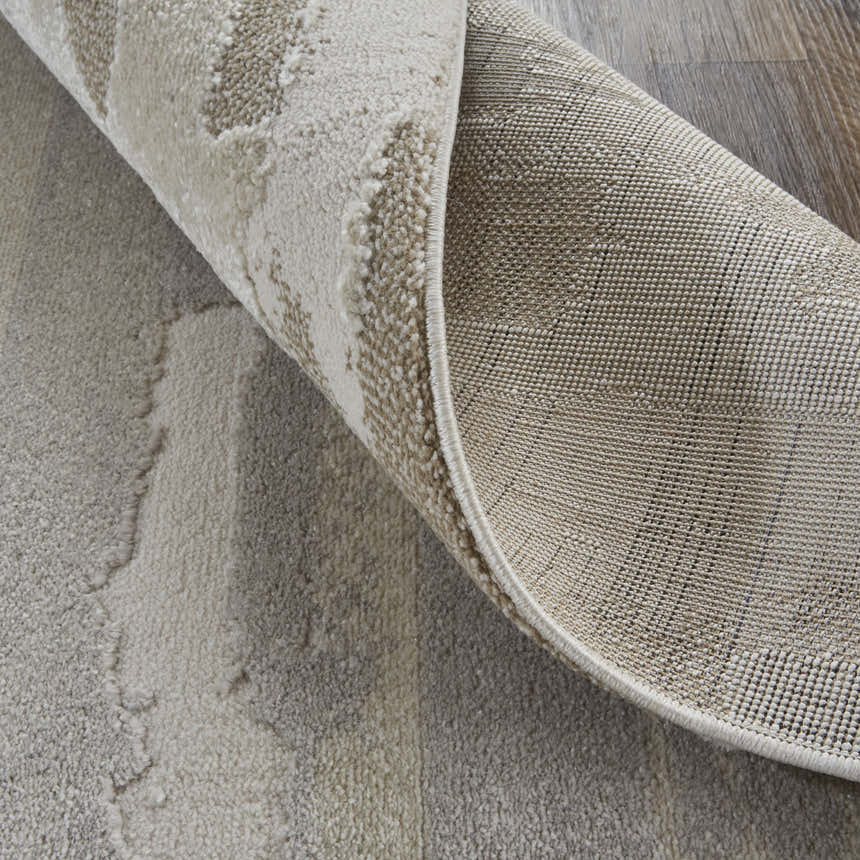 Close-up of the Feizy Vancouver rug showing its abstract ivory, tan, and brown pattern and machine-made construction. Fold